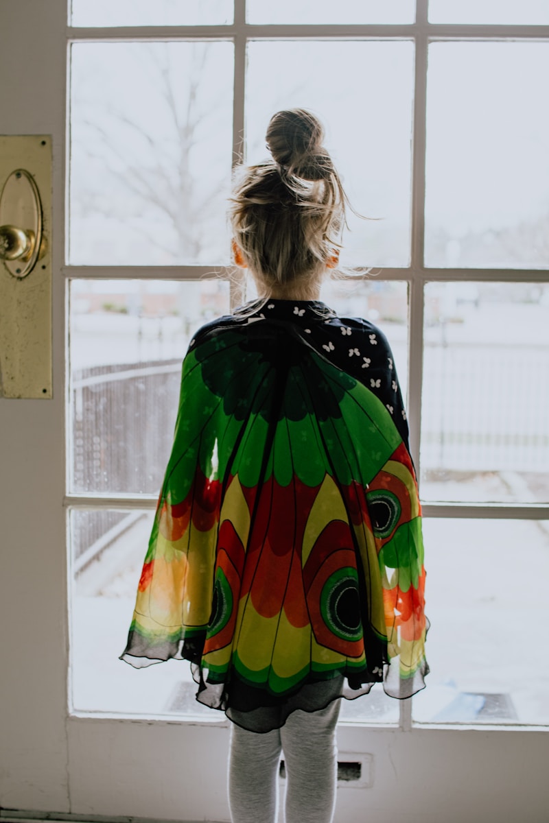 young girl in green orange and yellow fancy dress standing near window